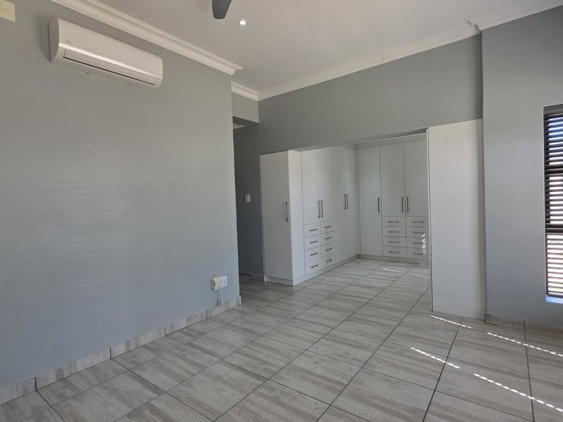 Spacious bedroom featuring neutral grey walls, tiled flooring, built-in cupboards, and a wall-mounted air conditioning unit.