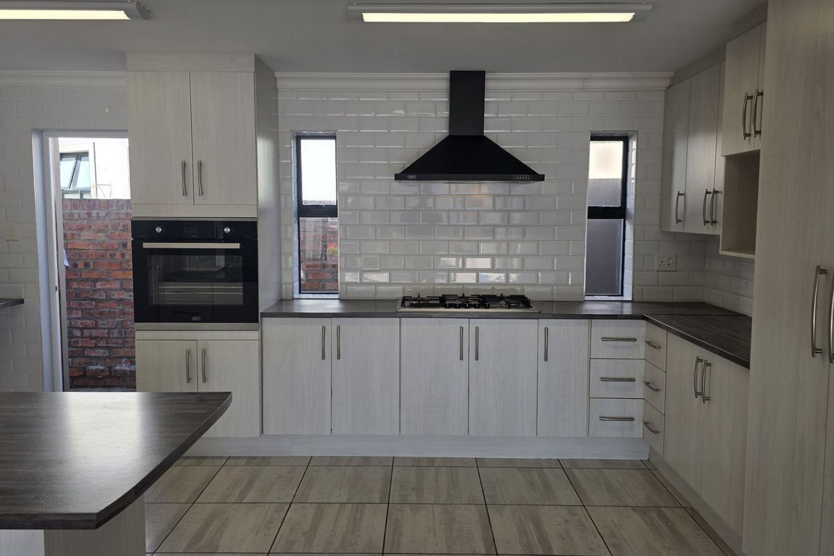 Modern kitchen featuring light wood-grain cabinetry, subway tile backsplash, built-in oven, gas hob, and dark laminate countertops with tiled flooring.
