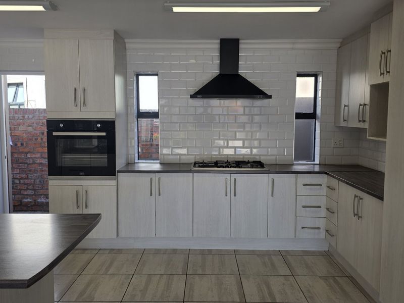 Modern kitchen featuring light wood-grain cabinetry, subway tile backsplash, built-in oven, gas hob, and dark laminate countertops with tiled flooring.