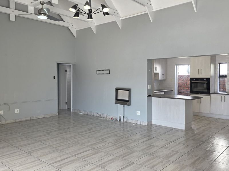Spacious open-plan living area featuring a vaulted ceiling with exposed rafters, tiled flooring, a built-in fireplace, and a modern kitchen with integrated appliances.