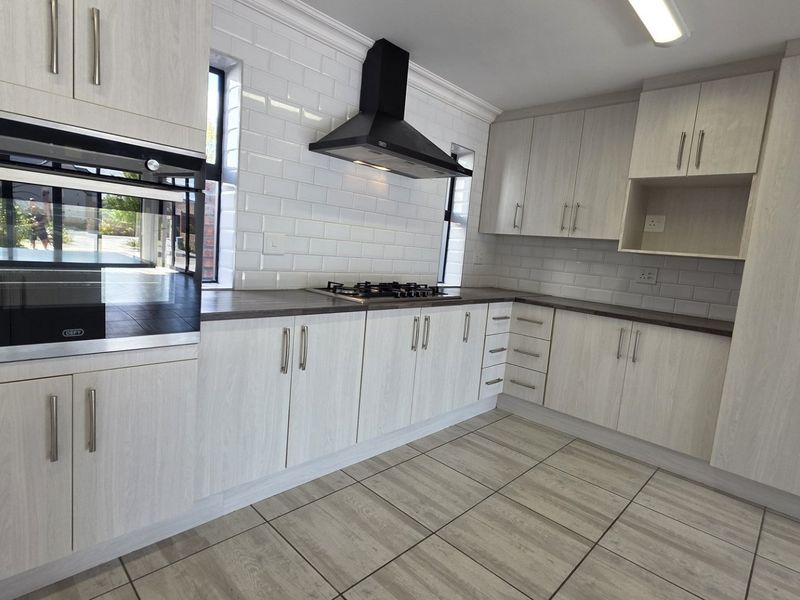 Modern kitchen featuring light wood-grain cabinetry, subway tile backsplash, built-in oven, gas hob, and extractor fan with neutral tiled flooring.