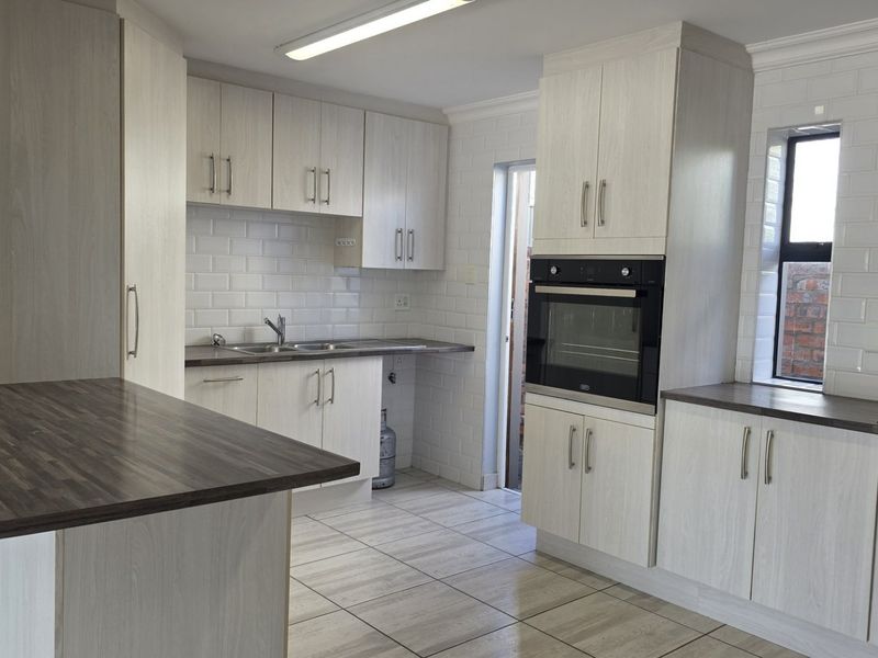Modern kitchen featuring light wood-grain cabinetry, subway tile backsplash, dark laminate countertops, built-in oven, gas hob, and tiled flooring.