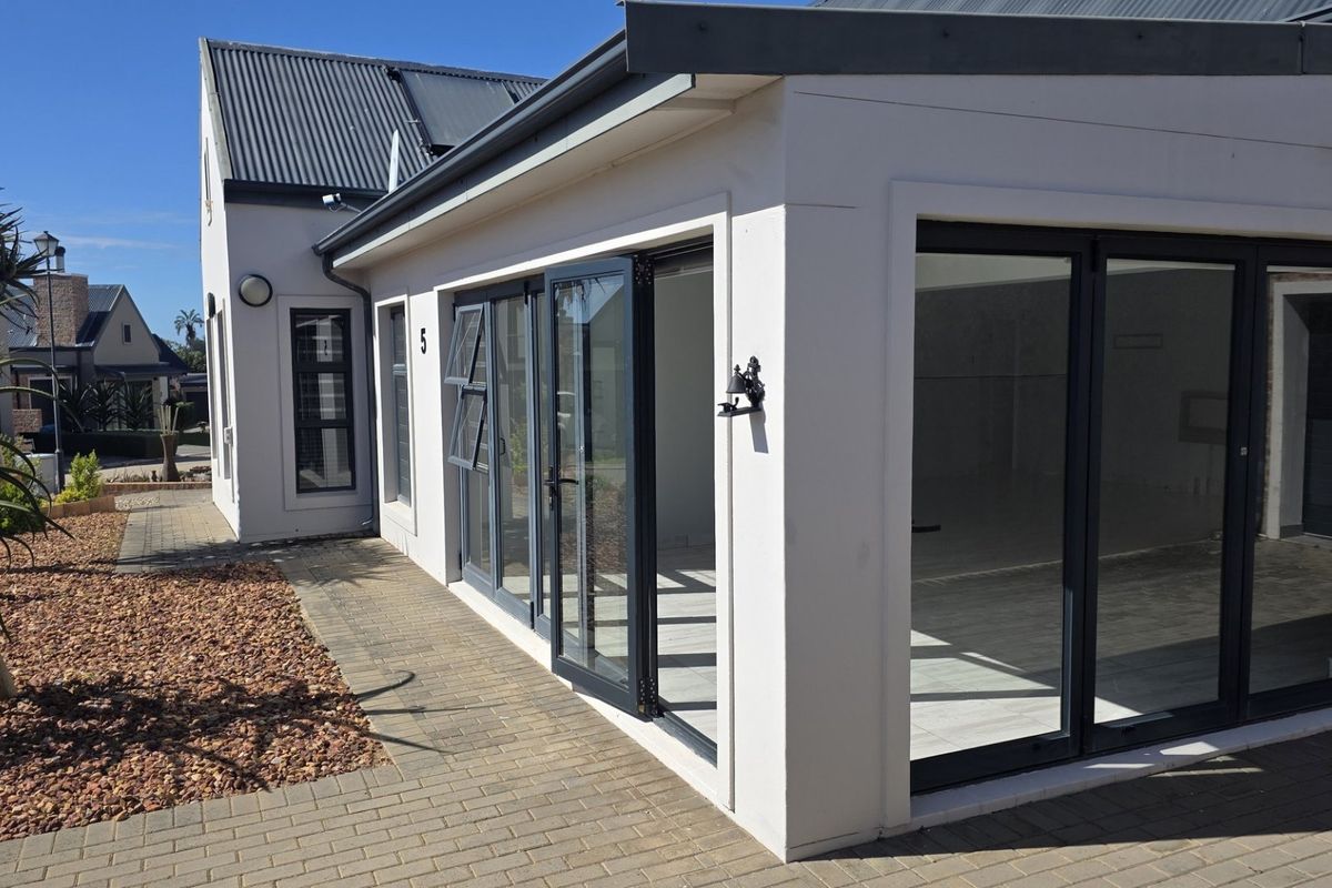 Rear view of the townhouse featuring modern aluminium stacker doors, paved pathways, and a well-maintained exterior facade.