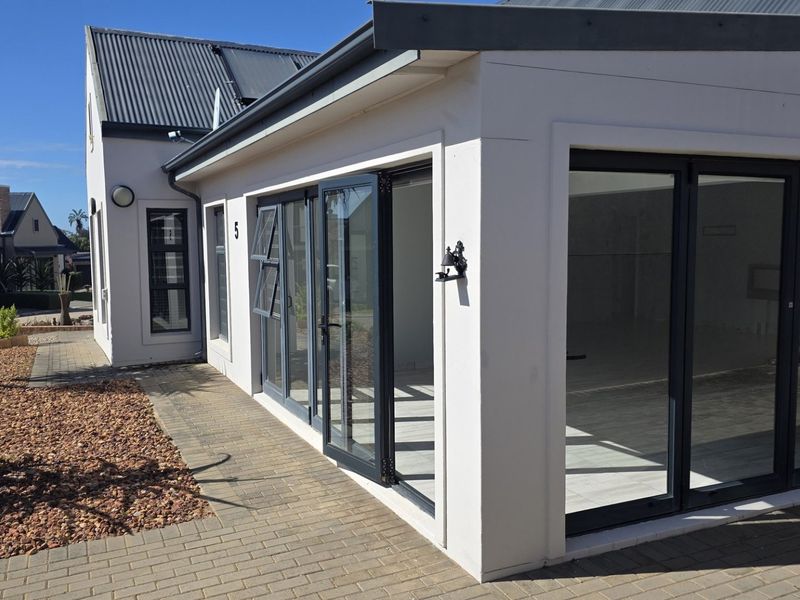 Rear view of the townhouse featuring modern aluminium stacker doors, paved pathways, and a well-maintained exterior facade.