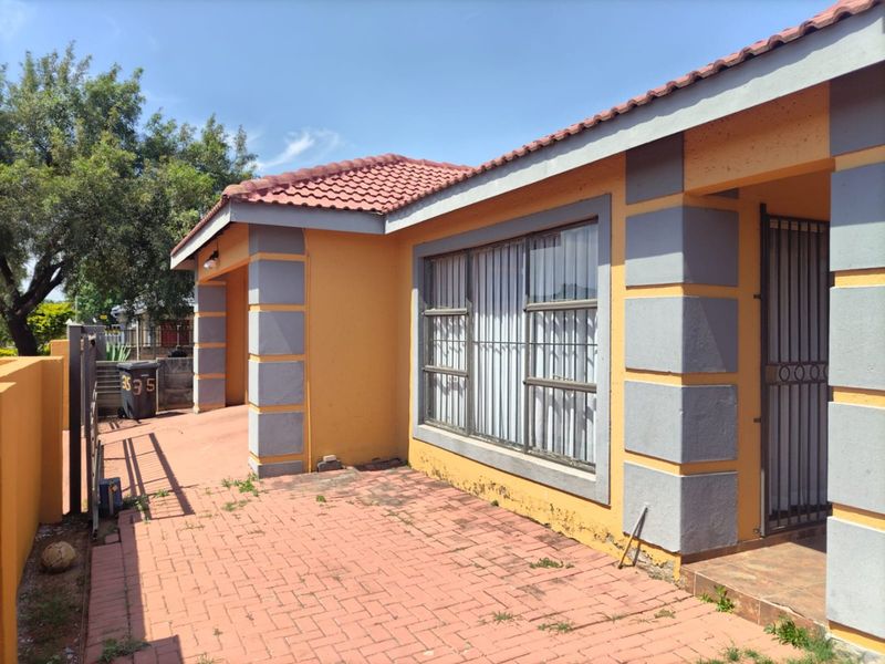 Front exterior view of the house featuring a paved driveway, tiled roof, and security features including metal bars and a gate.