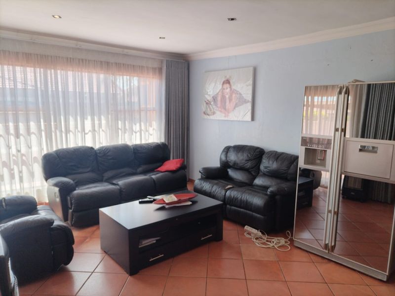 A spacious living room featuring terracotta floor tiles, recessed downlighting, and large windows with sheer curtains, offering a functional and well-lit living space.