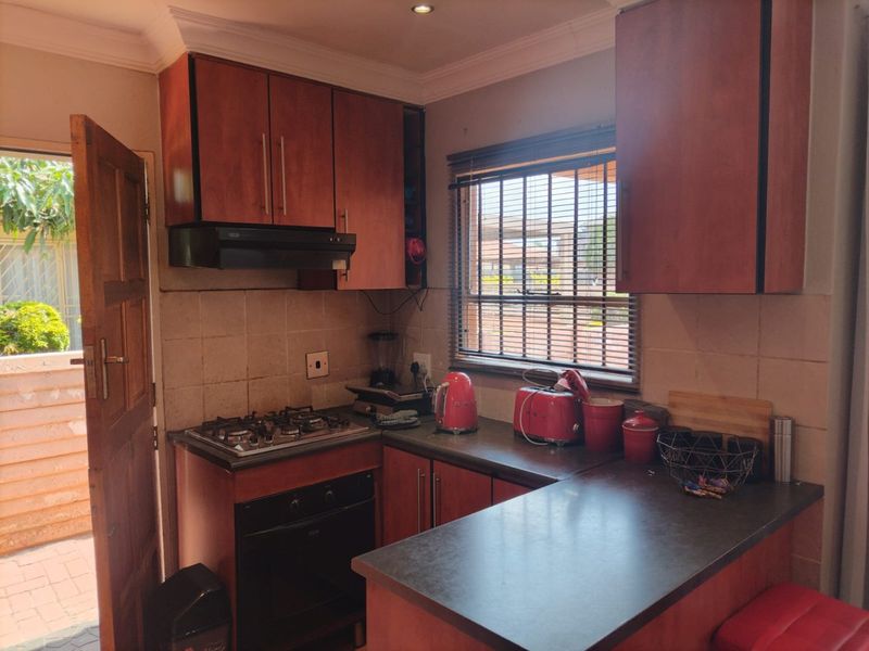 A functional kitchen featuring wooden cabinetry, a gas hob, built-in oven, and a tiled backsplash with direct access to the exterior.