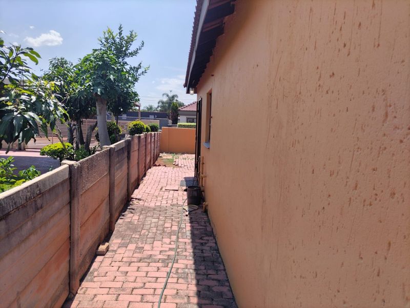 A side exterior walkway featuring paved flooring and a precast concrete boundary wall, showing signs of weathering on the exterior wall surface.
