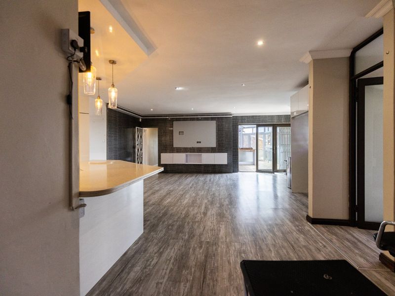 Spacious open-plan living area featuring modern laminate flooring, built-in media cabinetry, breakfast bar, and seamless access to the outdoor patio through sliding glass doors.