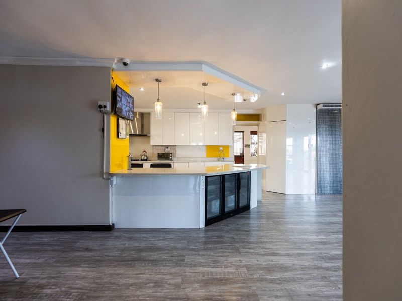 Modern open-plan kitchen featuring high-gloss white cabinetry, stone countertops, integrated under-counter refrigeration, and stylish pendant lighting, set against a vibrant yellow accent wall.