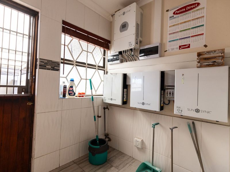Utility space featuring a wall-mounted solar inverter and battery storage system, with tiled finishes and a secure exterior access door.