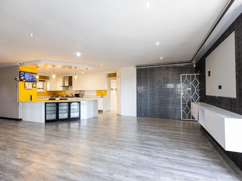 Spacious open-plan living area featuring a modern kitchen with island, integrated beverage coolers, and sleek finishes, flowing into a large, versatile living space.