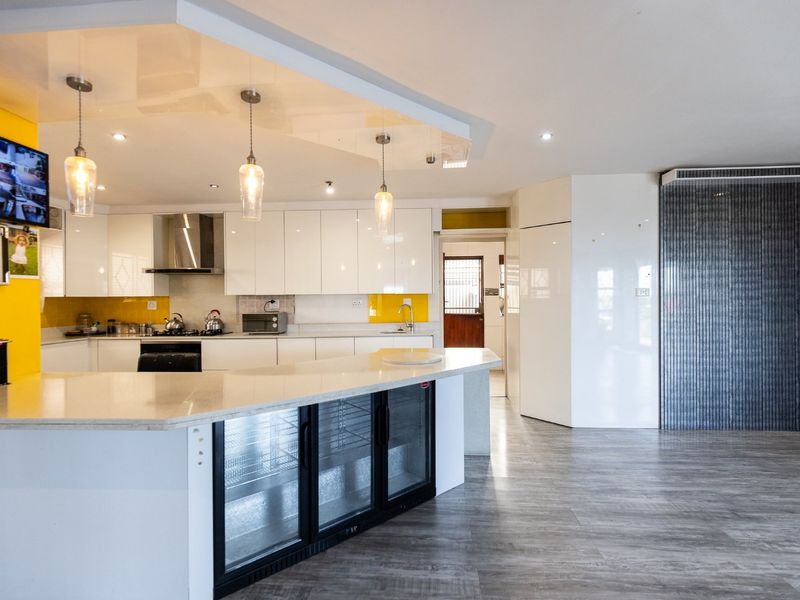Modern kitchen featuring high-gloss white cabinetry, stone countertops, integrated beverage fridge, and stylish pendant lighting, creating a clean and functional culinary space.