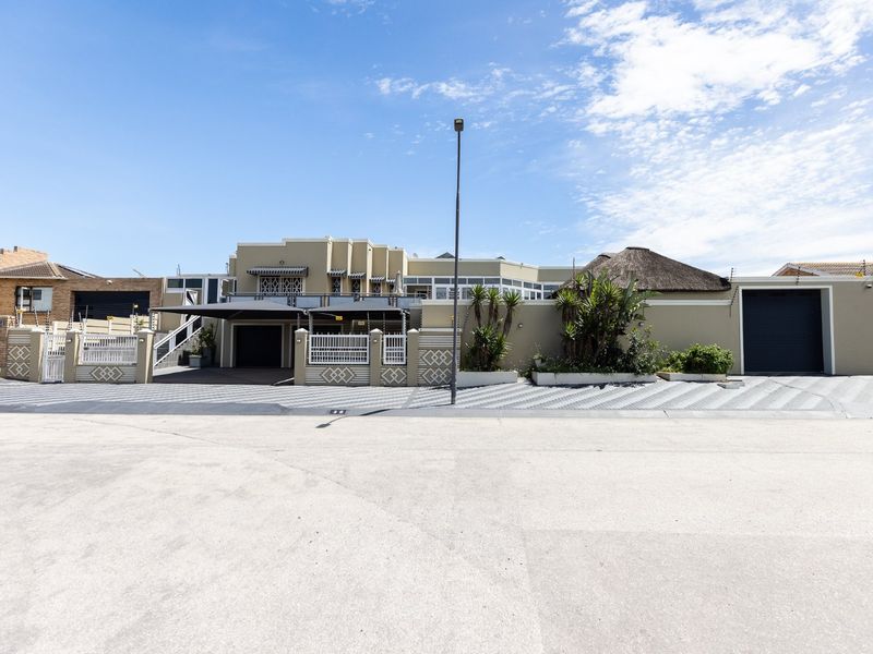 Front elevation of a well-maintained property featuring a paved driveway, carport, secure garage, and perimeter wall with electric fencing.