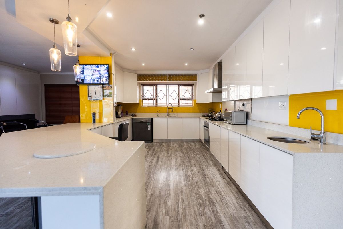 Modern kitchen featuring high-gloss white cabinetry, quartz countertops, integrated appliances, and a vibrant yellow backsplash, offering a clean and functional culinary space.