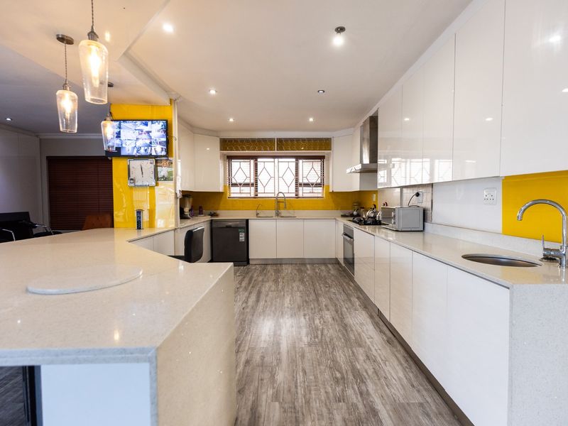 Modern kitchen featuring high-gloss white cabinetry, quartz countertops, integrated appliances, and a vibrant yellow backsplash, offering a clean and functional culinary space.