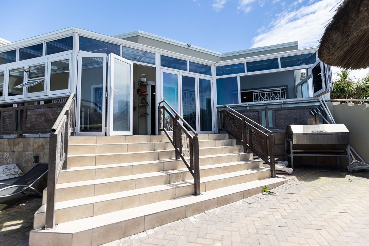 Rear exterior view featuring a tiled staircase leading to a glass-enclosed conservatory, paved patio area, and built-in braai facility.