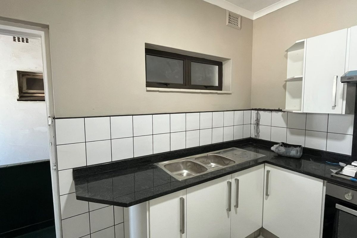 A functional kitchen featuring white cabinetry, a dark granite countertop with a double sink, built-in oven, and a tiled backsplash.