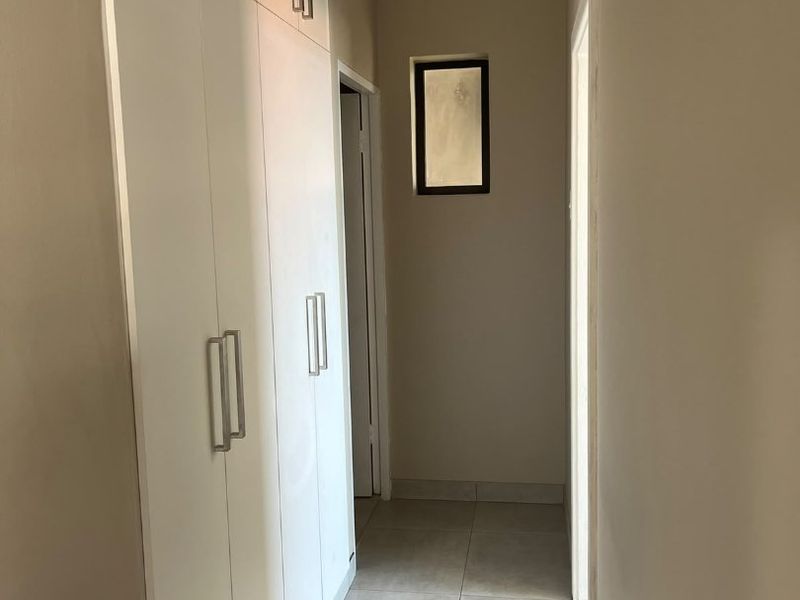 A functional hallway featuring built-in floor-to-ceiling cupboards and neutral tiled flooring, providing ample storage space.