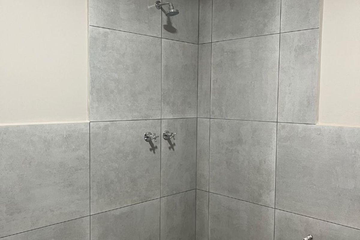 A modern walk-in shower area featuring large format grey wall tiles, a mosaic tiled floor, and chrome fixtures, currently awaiting a shower screen installation.