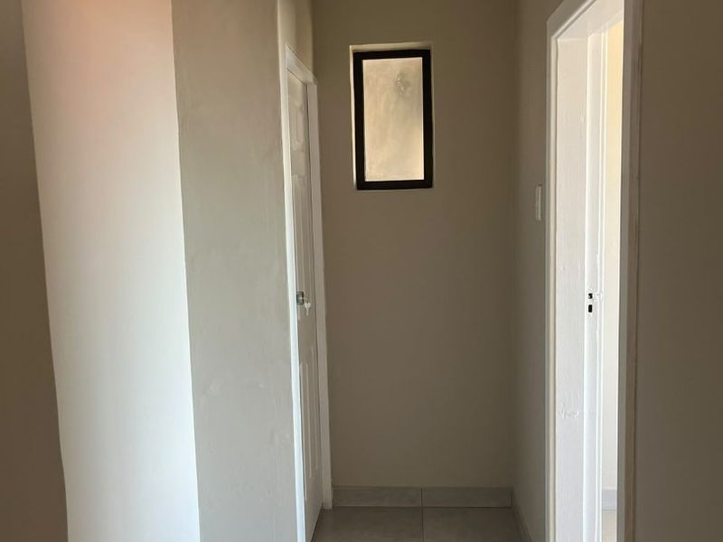 A neutral-toned hallway featuring tiled flooring, cove cornicing, and a small fixed window, currently awaiting final finishing touches to the skirting and wall base.