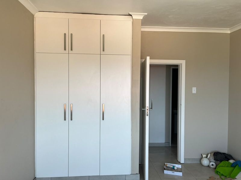 A bedroom featuring white built-in cupboards with modern handles, neutral wall paint, and coving detail.