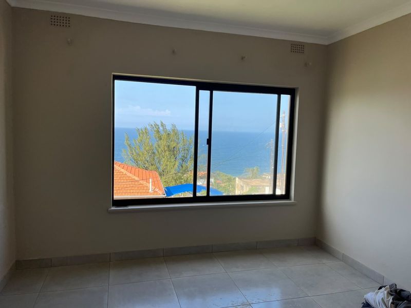 A bright, empty bedroom featuring neutral tiled flooring, a modern sliding window, and a scenic ocean view.