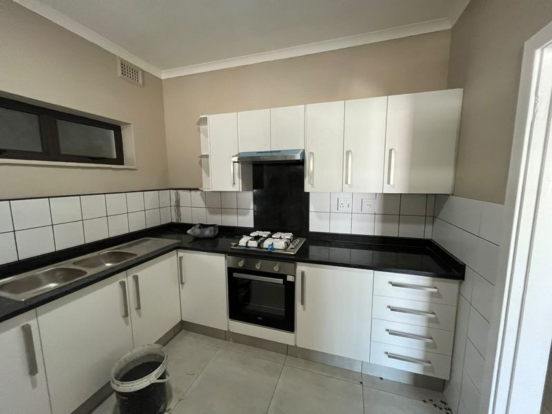 A functional kitchen featuring white cabinetry, black granite countertops, a built-in oven with gas hob, and tiled finishes throughout.