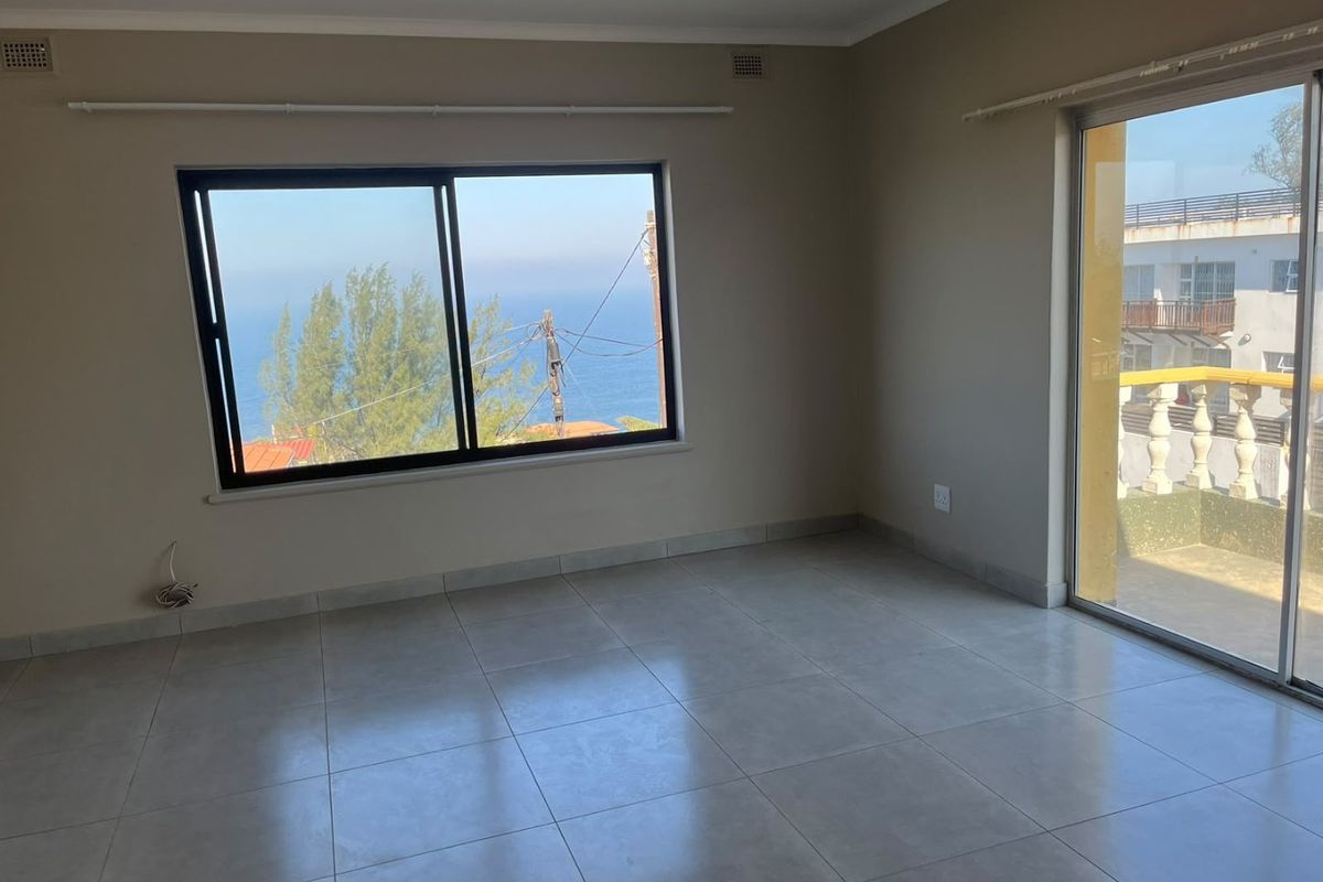 A bright, empty living area featuring neutral tiled flooring, large sliding glass doors, and expansive windows offering scenic coastal views.