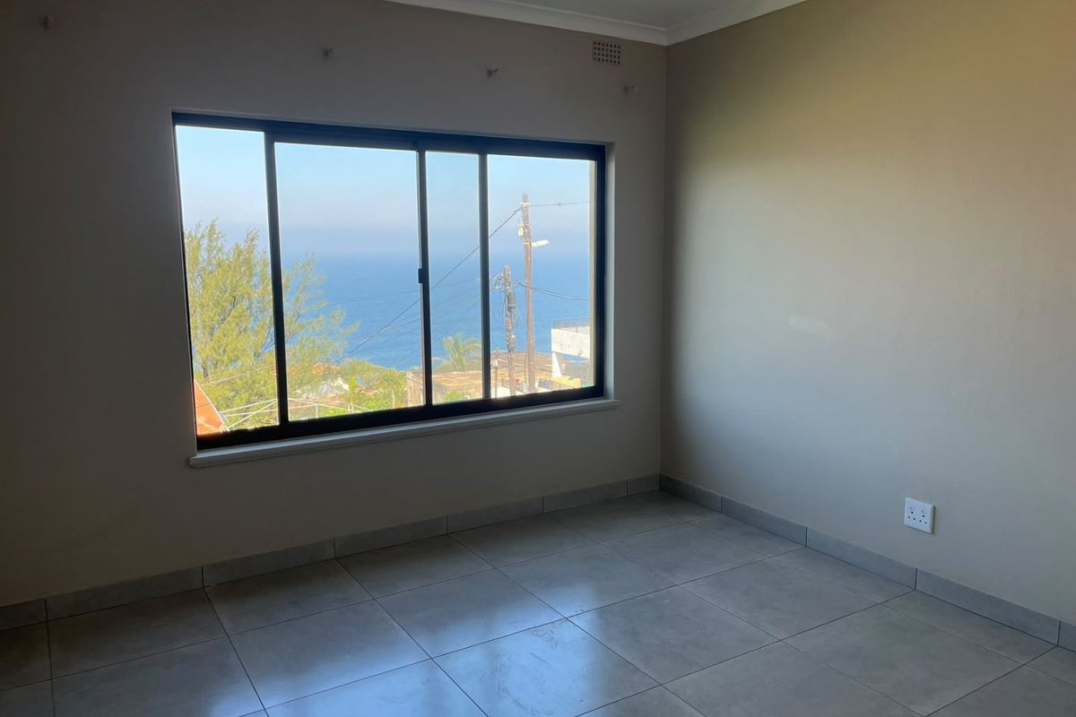 An empty bedroom featuring neutral tiled flooring and a large sliding window with a scenic ocean view.