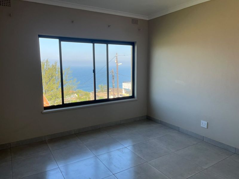 An empty bedroom featuring neutral tiled flooring and a large sliding window with a scenic ocean view.
