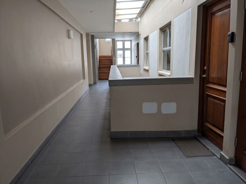 A clean and well-lit apartment hallway featuring tiled flooring, a skylight, and a wooden staircase leading to another level.
