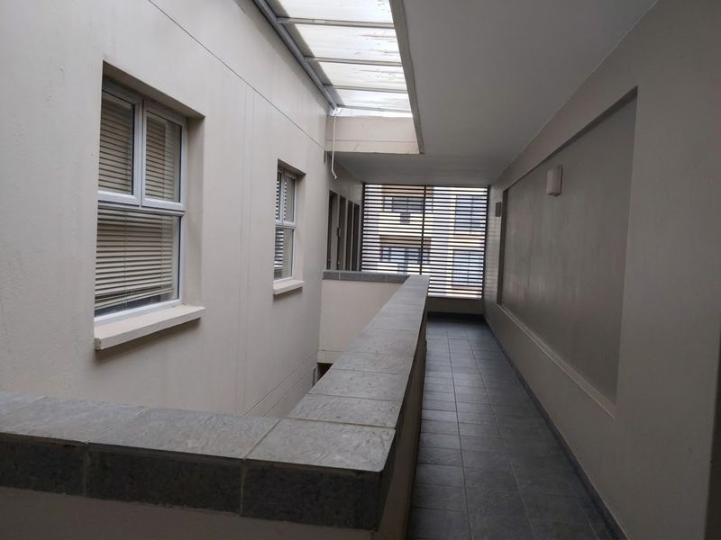A well-lit apartment hallway featuring tiled flooring, a skylight, and a tiled balustrade, providing access to adjacent units.