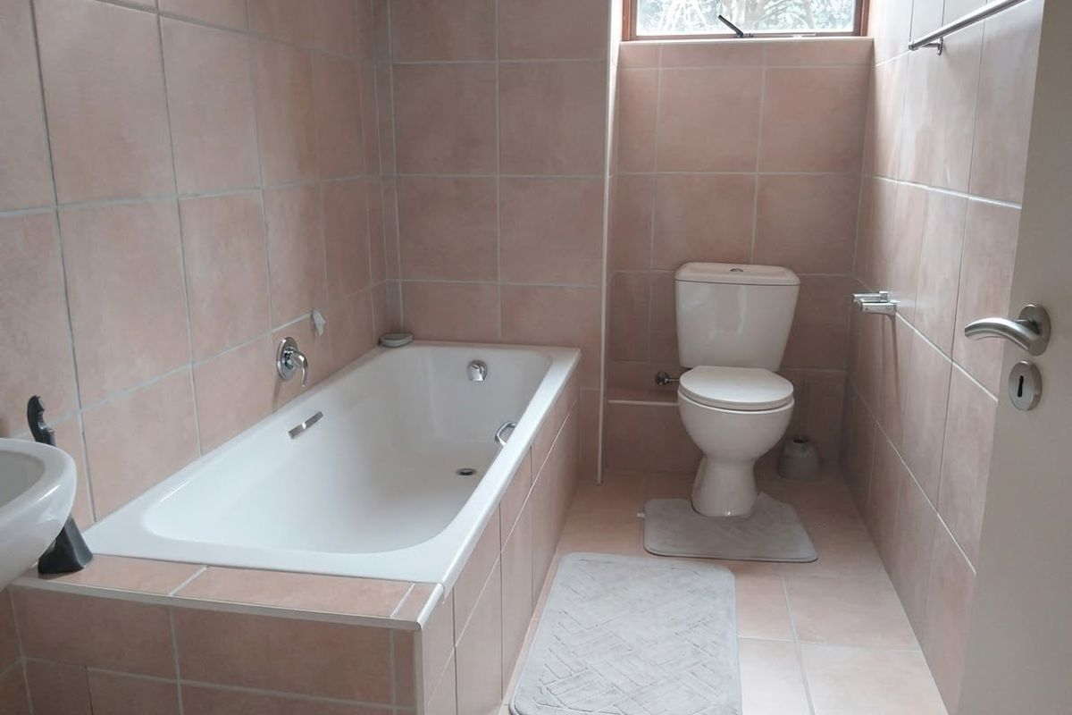 A functional bathroom featuring a built-in bathtub, toilet, and neutral wall and floor tiling, providing a clean and practical space.