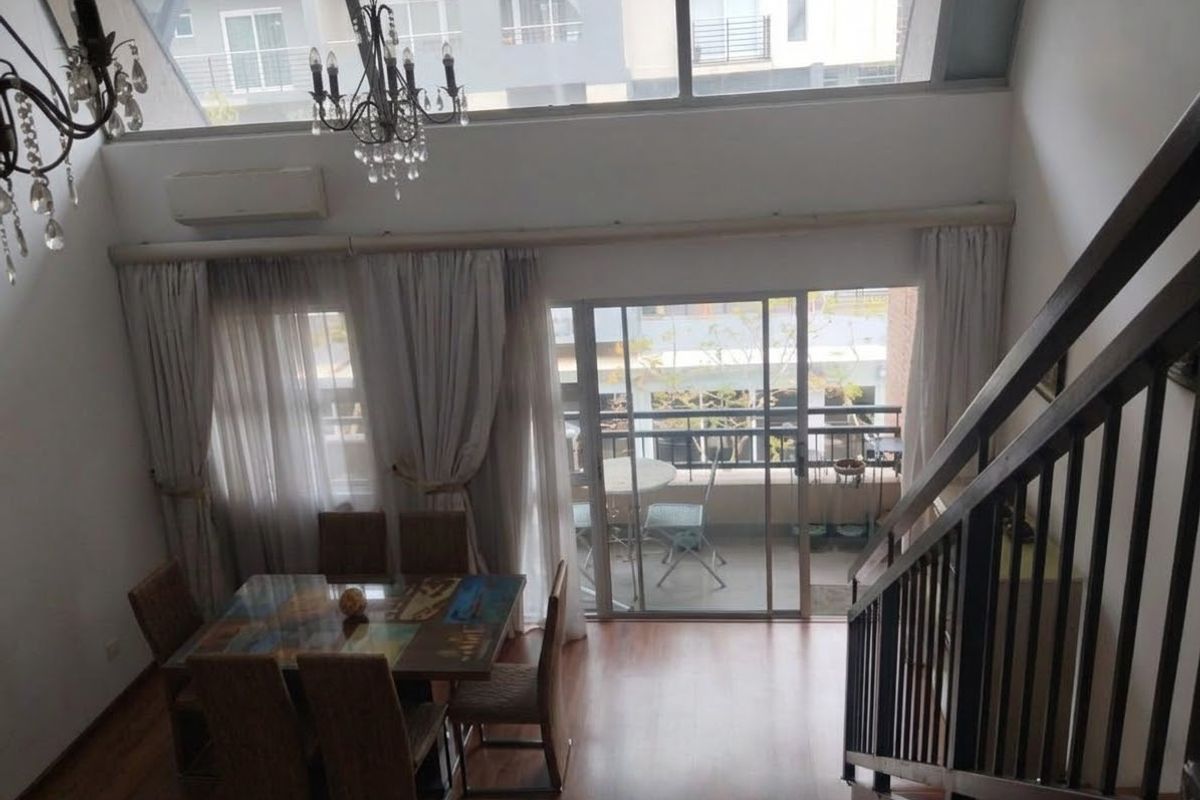 Spacious double-volume living area featuring laminate flooring, large windows, and a staircase with metal railing, leading out to a private balcony.