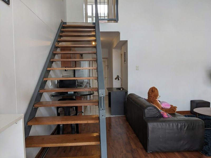 Open-plan living area featuring a modern open-tread staircase leading to a mezzanine level, with integrated kitchen space and durable laminate flooring throughout.