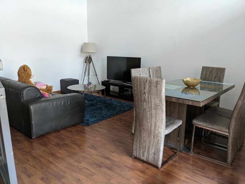 An open-plan living and dining area featuring dark wood-look laminate flooring and neutral wall finishes.
