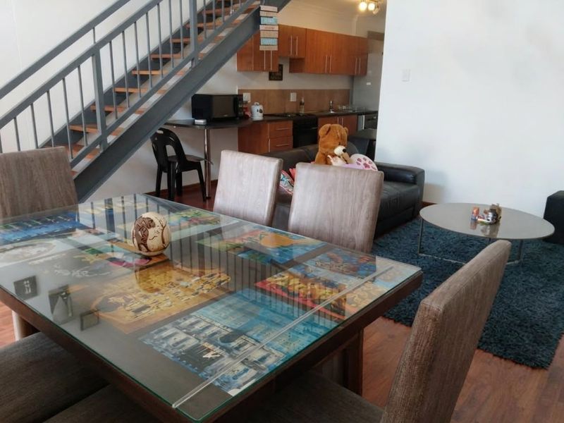 Open plan living and dining area featuring a staircase and a functional kitchen with wooden cabinetry and laminate flooring.
