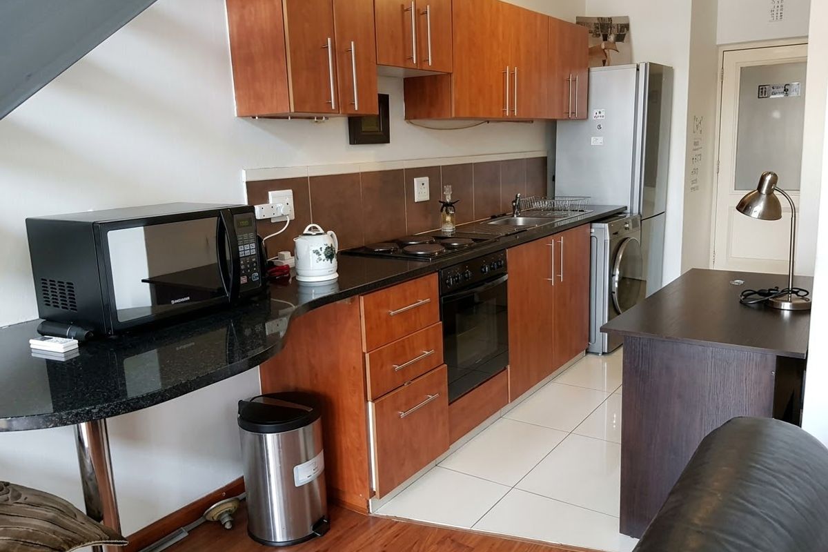 A functional kitchen featuring wooden cabinetry, granite countertops, an electric hob, and built-in oven, with a mix of tiled and laminate flooring.