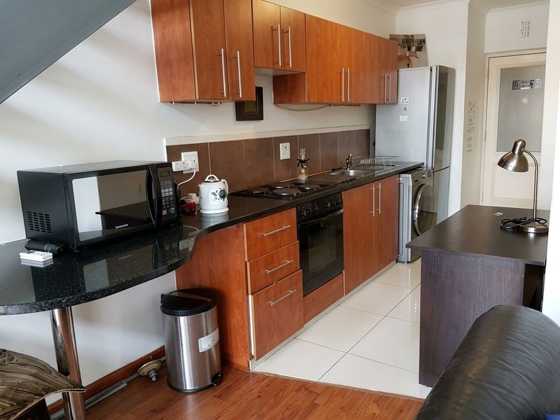 A functional kitchen featuring wooden cabinetry, granite countertops, an electric hob, and built-in oven, with a mix of tiled and laminate flooring.