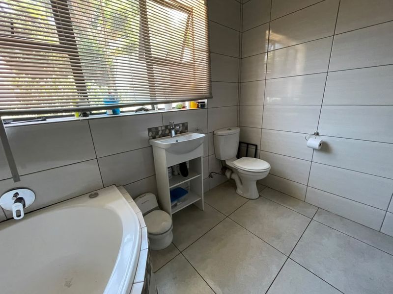 A clean, modern bathroom featuring large format wall and floor tiles, a pedestal basin, a toilet, and a built-in bathtub.