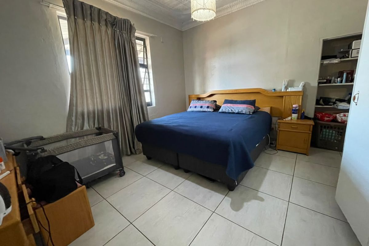 A bedroom featuring tiled flooring, ornate ceiling detailing, and built-in shelving, offering a functional space with potential for cosmetic updates.