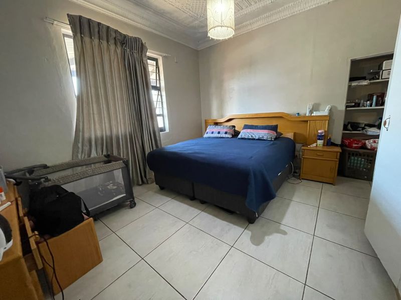 A bedroom featuring tiled flooring, ornate ceiling detailing, and built-in shelving, offering a functional space with potential for cosmetic updates.