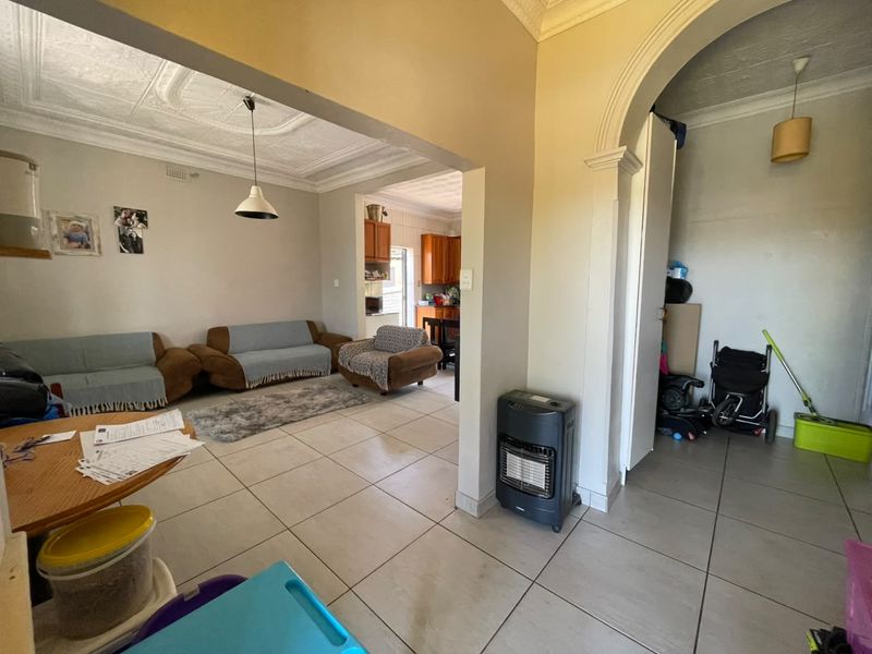 Open plan living area featuring tiled flooring, ornate ceiling details, and an arched transition leading to the kitchen area.