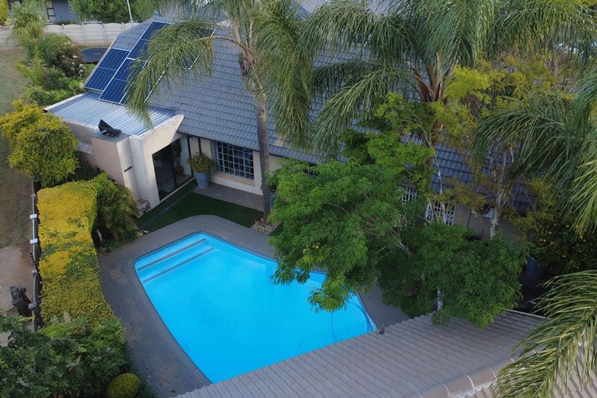 Aerial view of a residential property featuring a swimming pool, paved patio area, and solar panels installed on the tiled roof.