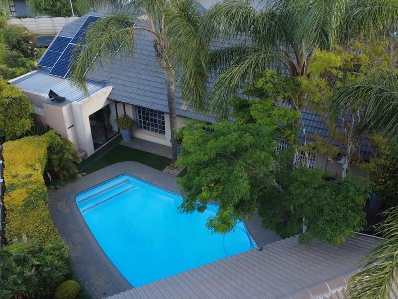 Aerial view of a residential property featuring a swimming pool, paved patio area, and solar panels installed on the tiled roof.