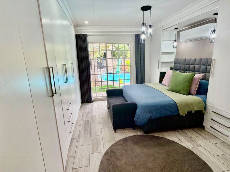 Modern bedroom featuring extensive built-in cabinetry, tiled flooring, air conditioning, and direct access to the outdoor pool area through a sliding glass door.
