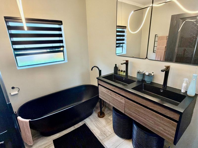 Modern bathroom featuring a sleek black freestanding bathtub, a contemporary double vanity with integrated sinks, and stylish matte black fixtures.