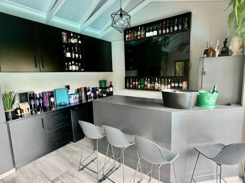 A modern, well-appointed home bar featuring sleek built-in cabinetry, a solid bar counter, vaulted ceilings, and a built-in fireplace.