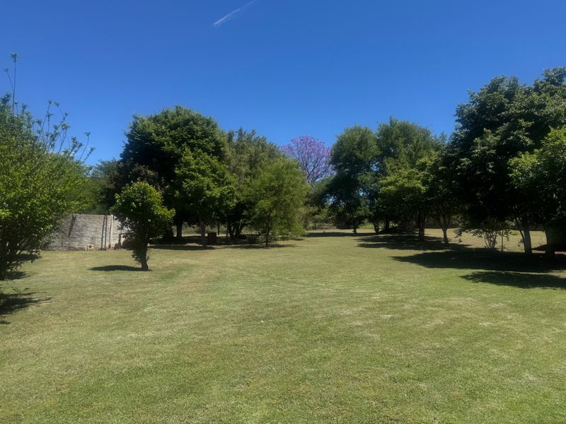 A spacious, well-maintained garden area featuring expansive green lawns and mature trees, providing a peaceful outdoor setting.